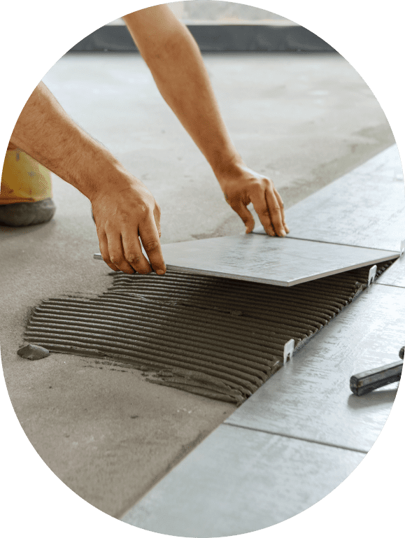 GettyImages-1158040145 A person laying a floor tile on adhesive with their hands, next to other installed tiles in a room.